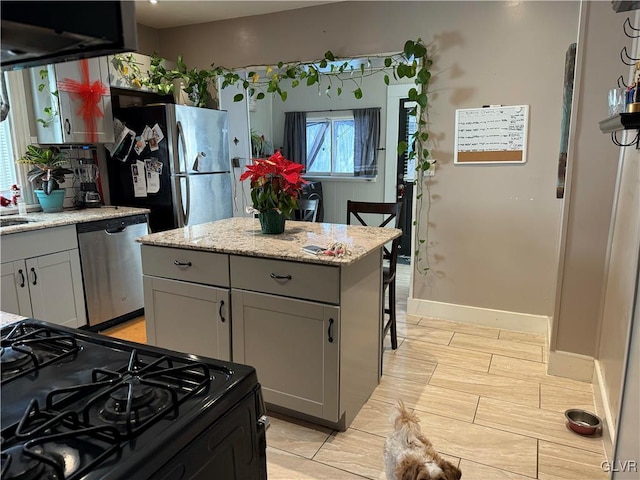 kitchen with gray cabinetry, light stone countertops, sink, a kitchen island, and appliances with stainless steel finishes