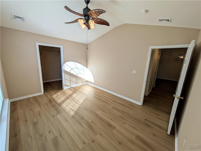 unfurnished bedroom featuring vaulted ceiling, a spacious closet, ceiling fan, light wood-type flooring, and a closet