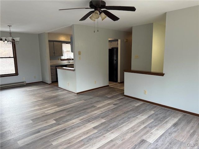 unfurnished living room featuring ceiling fan with notable chandelier, a baseboard radiator, light hardwood / wood-style flooring, and sink