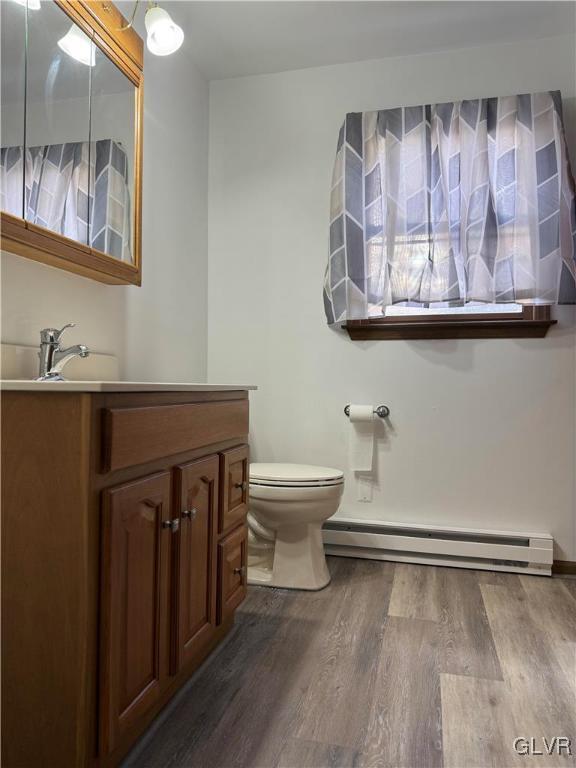 bathroom with vanity, toilet, wood-type flooring, and baseboard heating