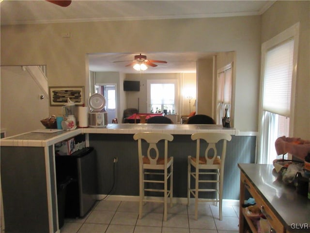 kitchen featuring kitchen peninsula, ceiling fan, ornamental molding, and light tile patterned flooring