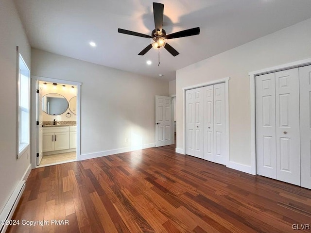 unfurnished bedroom featuring multiple closets, ensuite bathroom, hardwood / wood-style floors, and ceiling fan