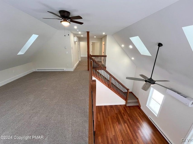 additional living space with vaulted ceiling with skylight, ceiling fan, dark hardwood / wood-style floors, and a baseboard heating unit