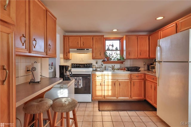 kitchen with sink, a kitchen breakfast bar, backsplash, white appliances, and light tile patterned floors