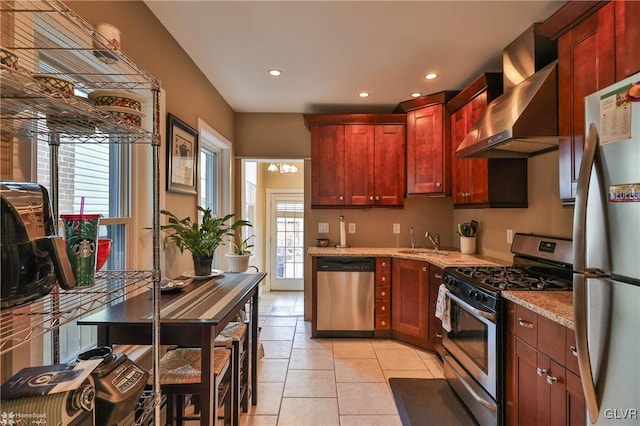 kitchen with a wealth of natural light, light stone countertops, sink, wall chimney exhaust hood, and appliances with stainless steel finishes