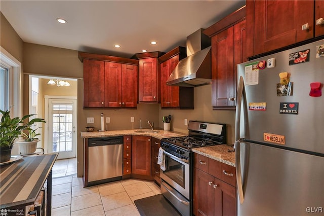 kitchen with light stone countertops, wall chimney range hood, appliances with stainless steel finishes, and an inviting chandelier