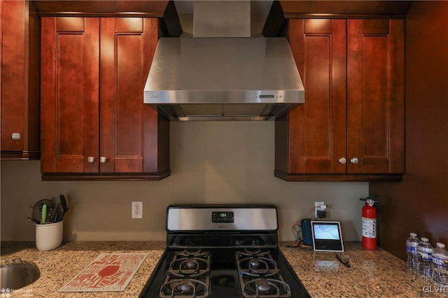 kitchen with black gas range oven, light stone countertops, and wall chimney range hood