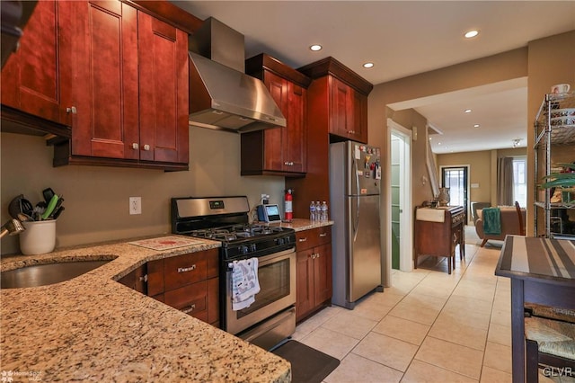 kitchen with sink, wall chimney exhaust hood, light stone counters, light tile patterned floors, and appliances with stainless steel finishes