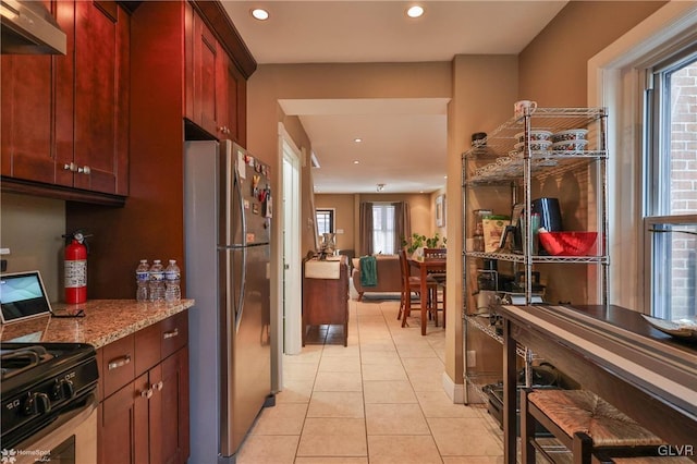 kitchen featuring stainless steel refrigerator, light stone countertops, range hood, black range, and light tile patterned floors