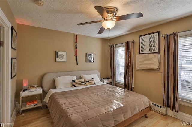 bedroom with a textured ceiling, light wood-type flooring, baseboard heating, and ceiling fan