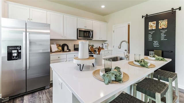 kitchen with a breakfast bar, white cabinets, a center island with sink, sink, and appliances with stainless steel finishes