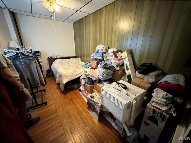 bedroom featuring hardwood / wood-style floors, a drop ceiling, wood walls, and ceiling fan