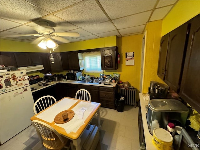 kitchen featuring radiator heating unit, dark brown cabinets, white fridge, and a drop ceiling