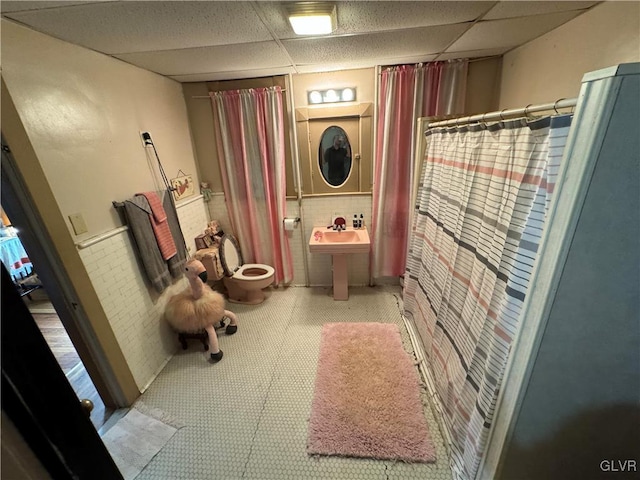 bathroom with toilet, a drop ceiling, and tile walls