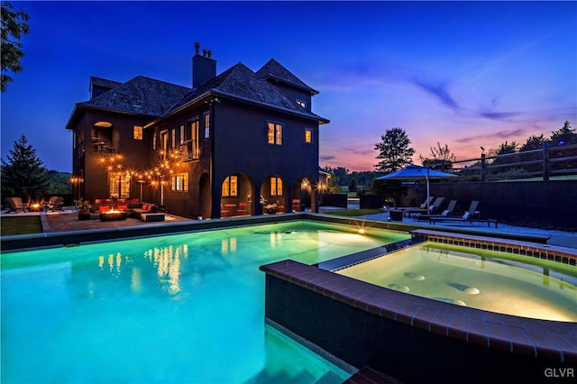 pool at dusk with an in ground hot tub, a patio, and an outdoor hangout area