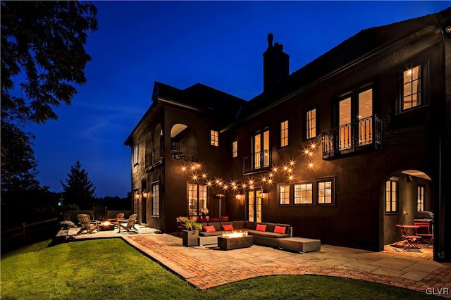 back house at night with a yard, a balcony, an outdoor living space with a fire pit, and a patio