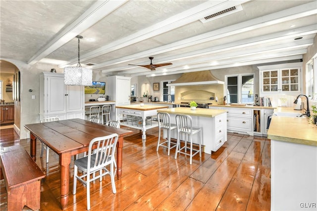 kitchen featuring beam ceiling, white cabinetry, ceiling fan, decorative light fixtures, and custom range hood