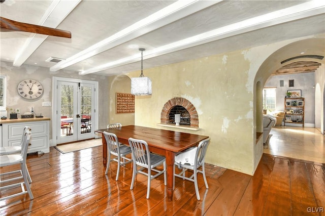 dining space featuring french doors, beamed ceiling, wood-type flooring, and a brick fireplace