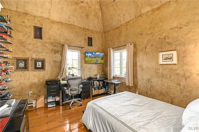 bedroom with multiple windows, hardwood / wood-style floors, and a towering ceiling