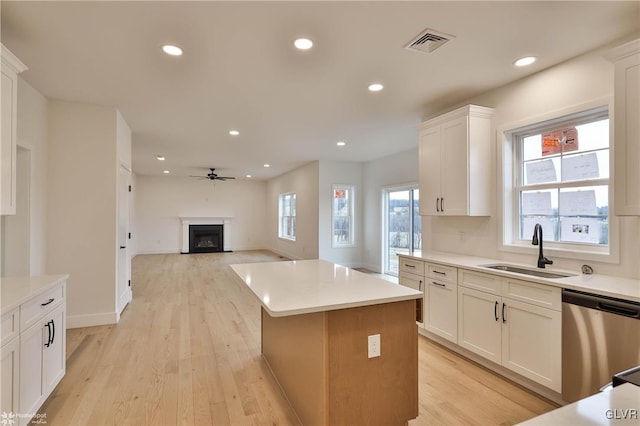 kitchen with stainless steel dishwasher, a kitchen island, ceiling fan, sink, and white cabinetry