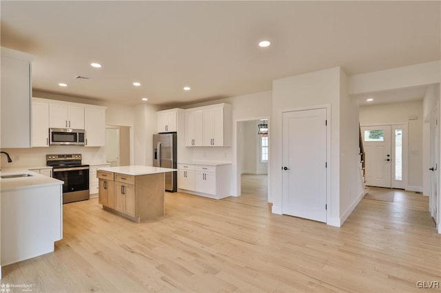 kitchen featuring white cabinetry, sink, a center island, light hardwood / wood-style floors, and appliances with stainless steel finishes