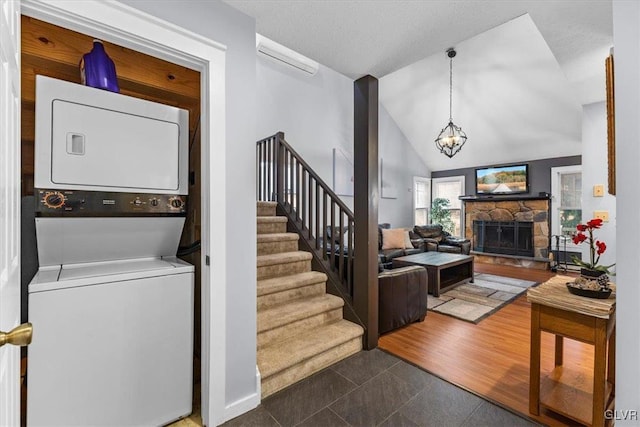 interior space with an inviting chandelier, a stone fireplace, dark tile patterned floors, and stacked washer and clothes dryer