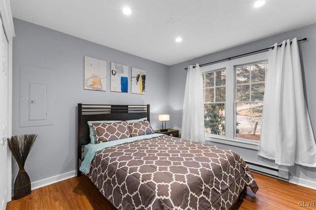 bedroom with multiple windows, electric panel, hardwood / wood-style flooring, and baseboard heating