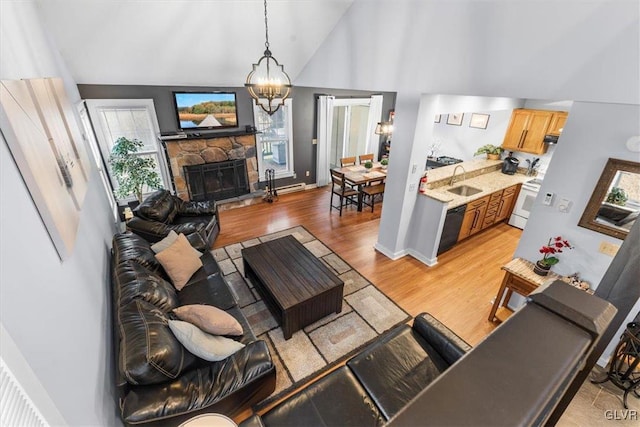 living room featuring high vaulted ceiling, a stone fireplace, sink, light hardwood / wood-style flooring, and a notable chandelier