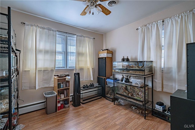 miscellaneous room featuring a baseboard heating unit, ceiling fan, and wood-type flooring