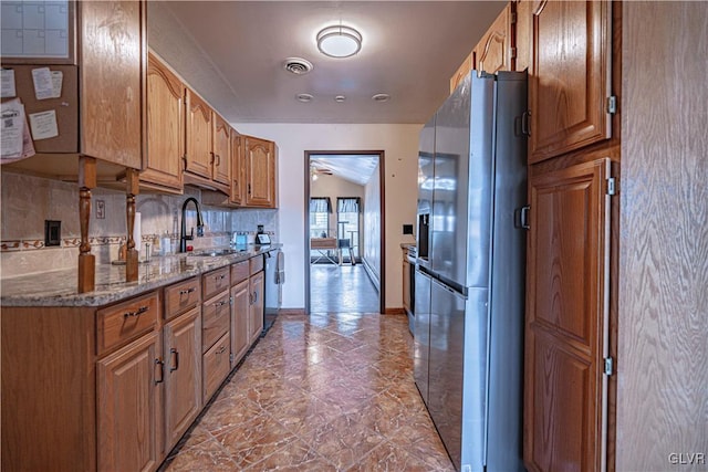 kitchen featuring lofted ceiling, ceiling fan, stainless steel refrigerator with ice dispenser, sink, and stone countertops