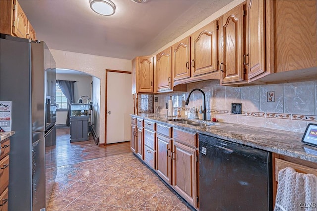 kitchen with dishwasher, decorative backsplash, sink, stone countertops, and stainless steel refrigerator