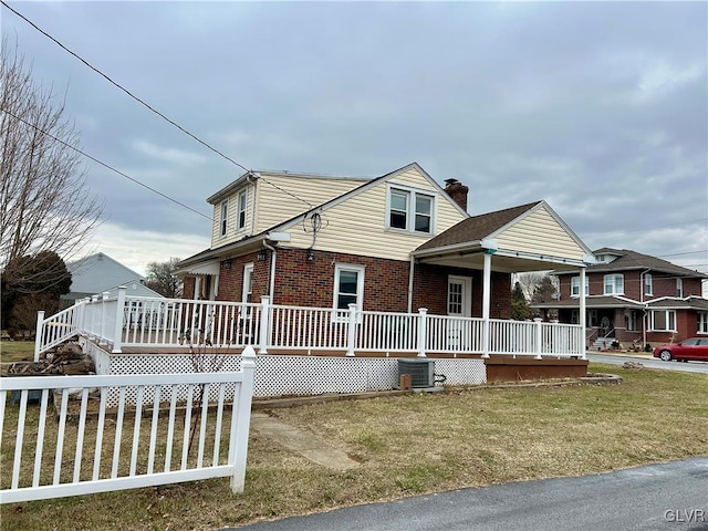 view of front facade featuring cooling unit, covered porch, and a front yard