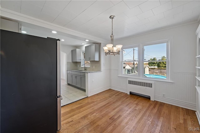 unfurnished dining area featuring radiator, sink, a notable chandelier, crown molding, and light hardwood / wood-style floors