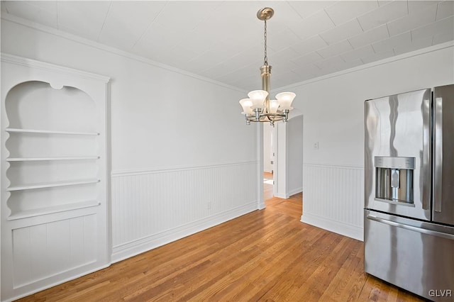 unfurnished dining area featuring hardwood / wood-style floors, crown molding, built in features, and a chandelier