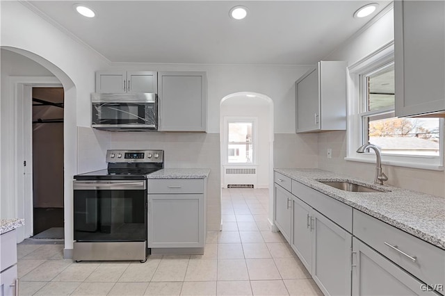 kitchen with radiator, sink, light stone counters, gray cabinets, and appliances with stainless steel finishes