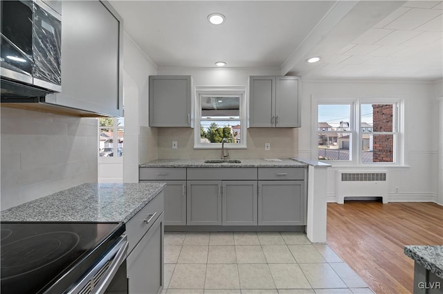 kitchen with radiator, light stone countertops, sink, gray cabinetry, and plenty of natural light