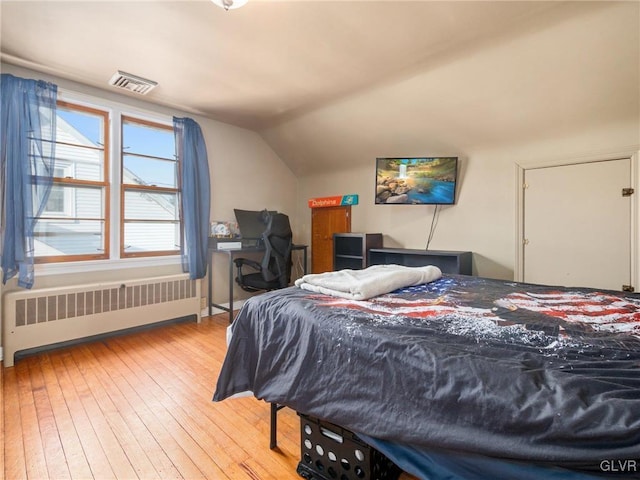 bedroom featuring light wood-type flooring, radiator, and lofted ceiling