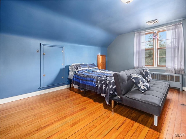 bedroom featuring hardwood / wood-style flooring, radiator heating unit, and vaulted ceiling