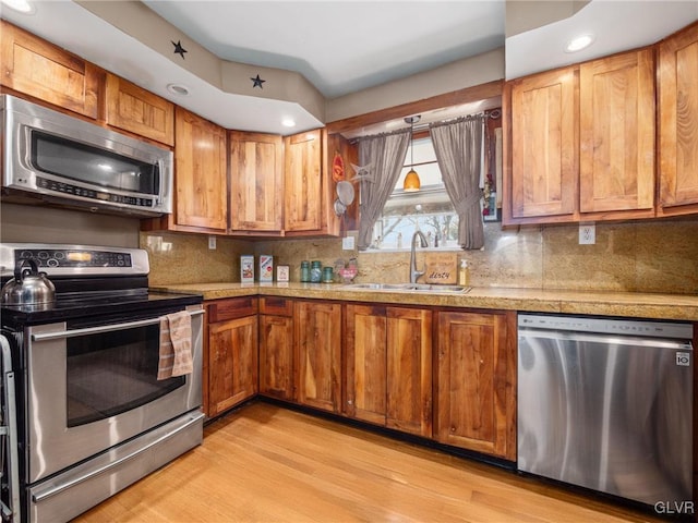 kitchen with decorative backsplash, appliances with stainless steel finishes, light hardwood / wood-style flooring, and sink