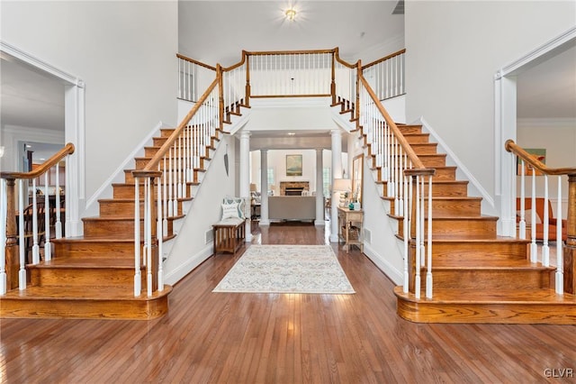 foyer featuring ornate columns, a towering ceiling, wood-type flooring, and ornamental molding