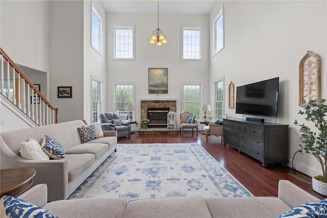 living room featuring dark hardwood / wood-style flooring, a stone fireplace, a high ceiling, and a chandelier