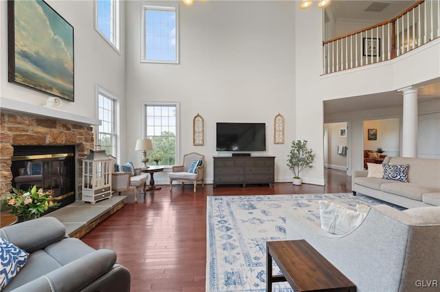 living room featuring decorative columns, a stone fireplace, dark hardwood / wood-style flooring, and a high ceiling