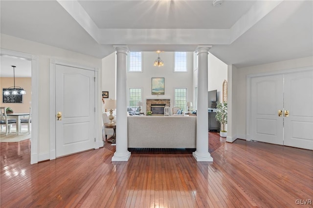 entrance foyer with hardwood / wood-style floors, a notable chandelier, a stone fireplace, and decorative columns