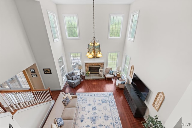 living room featuring a towering ceiling, an inviting chandelier, a stone fireplace, and dark wood-type flooring