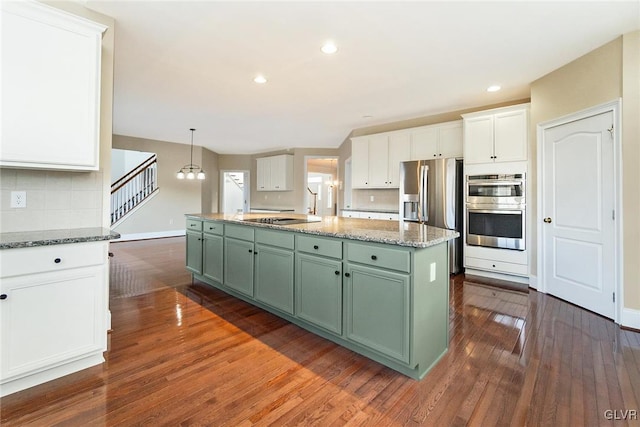 kitchen featuring dark wood-type flooring, a center island with sink, stainless steel appliances, and green cabinetry