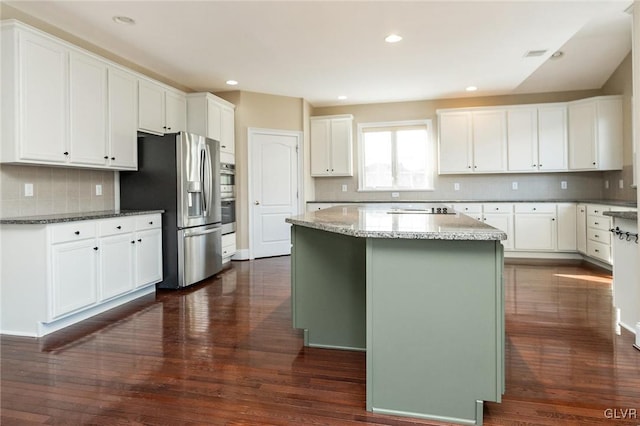 kitchen featuring light stone countertops, white cabinets, dark hardwood / wood-style floors, a kitchen island, and appliances with stainless steel finishes