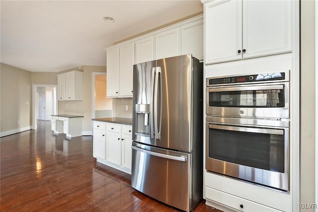 kitchen with dark hardwood / wood-style flooring, dark stone countertops, decorative backsplash, white cabinets, and appliances with stainless steel finishes