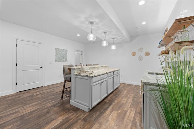 kitchen with pendant lighting, gray cabinetry, dark wood-type flooring, a center island with sink, and light stone countertops