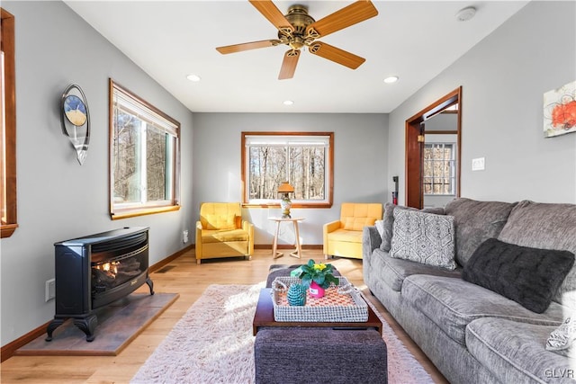 living room with light hardwood / wood-style floors, a wood stove, and ceiling fan