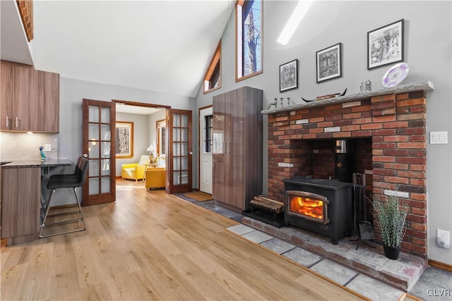 living room featuring a wood stove, french doors, high vaulted ceiling, and light hardwood / wood-style flooring